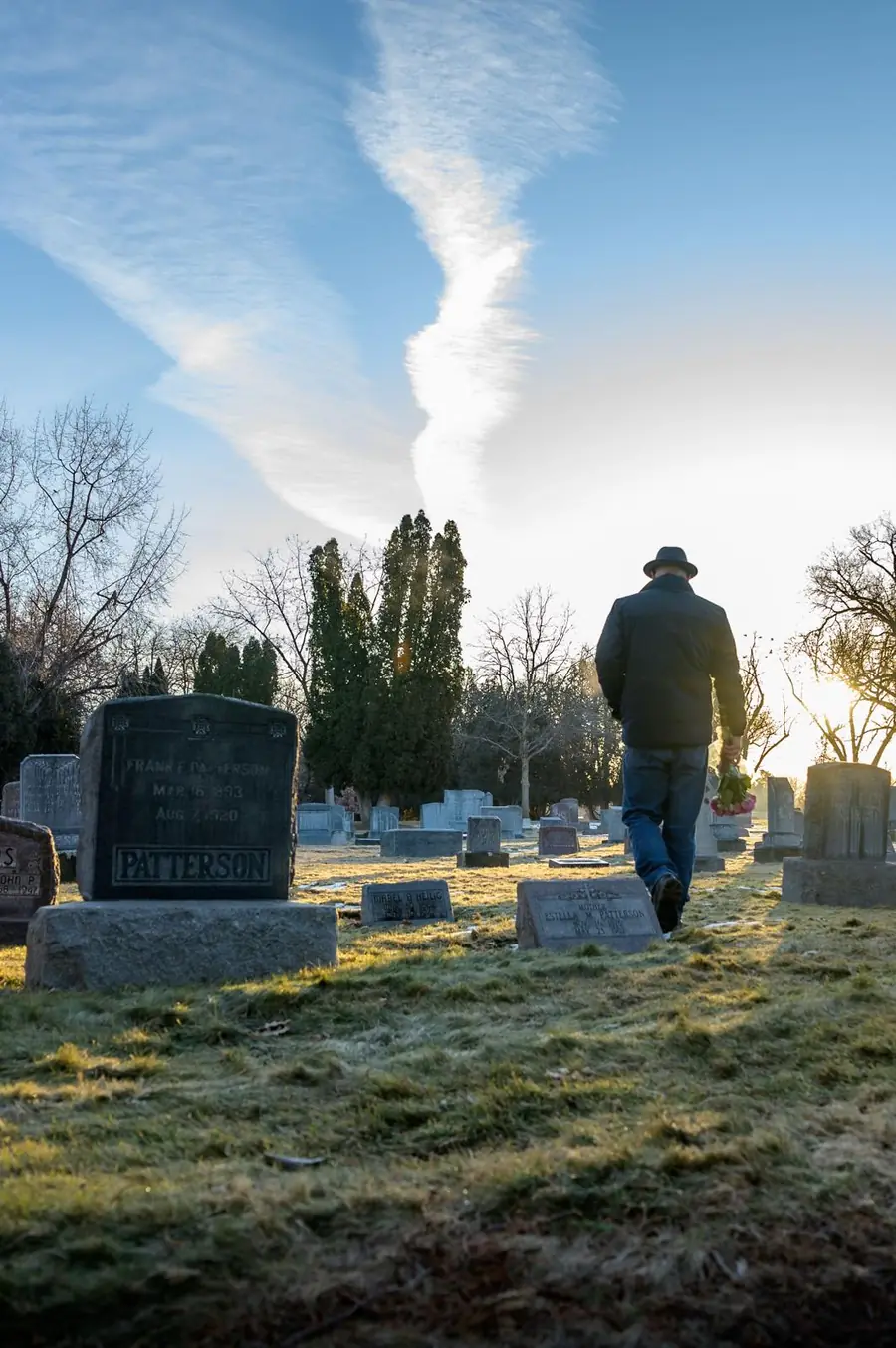 Man walking through a cemetery at sunrise carrying flowers