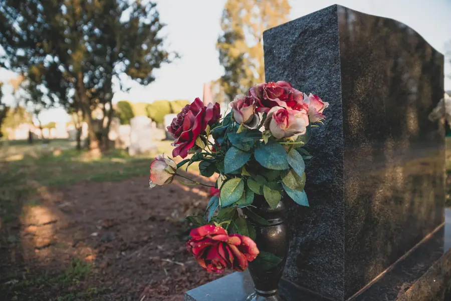 Roses in a black granite vase beside a polished headstone