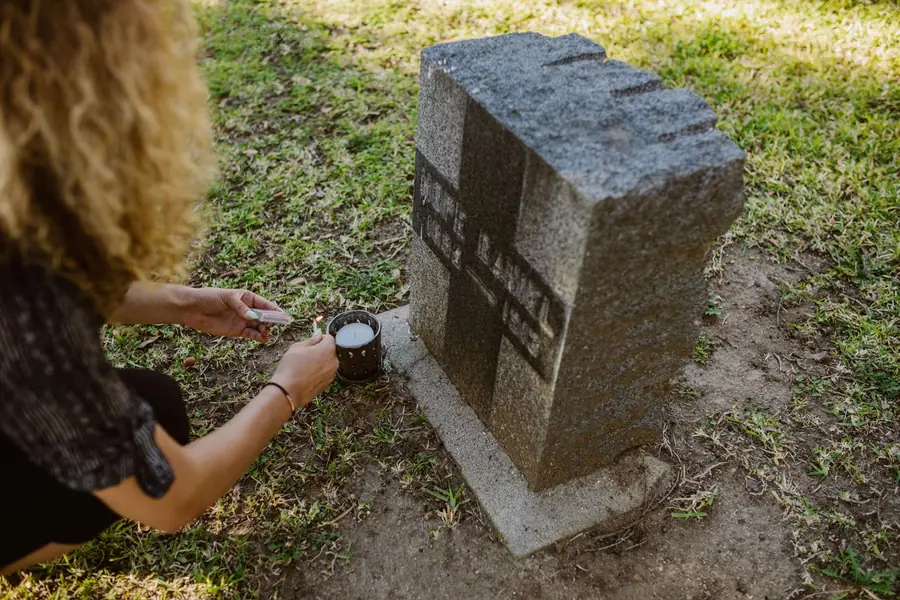 Woman lighting a candle beside a granite monument